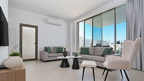 Una sala de estar moderna con sofá, sillón, mesa de centro y vistas amplias a través de grandes ventanales.