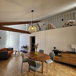 Ein zeitgemäßer Wohnraum mit einem Holzespeisetisch, grauen Polsterstühlen, einem Fernseher und einer Treppe zu einer oberen Ebene.
