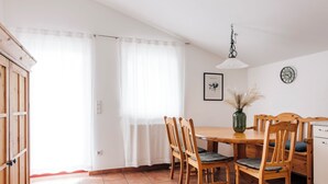En matplats med ett träbord och stolar, en vas med torkade växter, en klocka på väggen och en dörr med en träram.