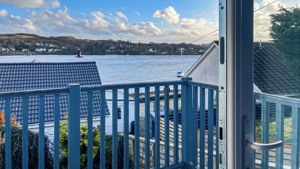 En balkong med utsikt över en vattenyta, hus i bakgrunden och en klar himmel.