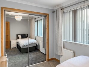 A bedroom with a bed, a nightstand, a radiator, a window with blinds, and a door leading to another room.