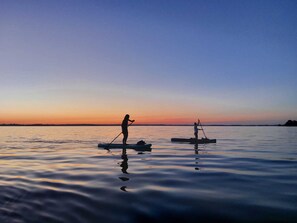 Ruhige Wasserfläche mit zwei Stand-Up-Paddleboards, eines davon wird von einer Person betreten, das andere von einer paddelnden Person gesteuert.