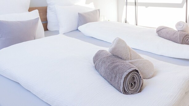 Een hotelkamer met twee bedden, wit beddengoed, een houten balk in het plafond, een hanglamp en een raam met uitzicht.