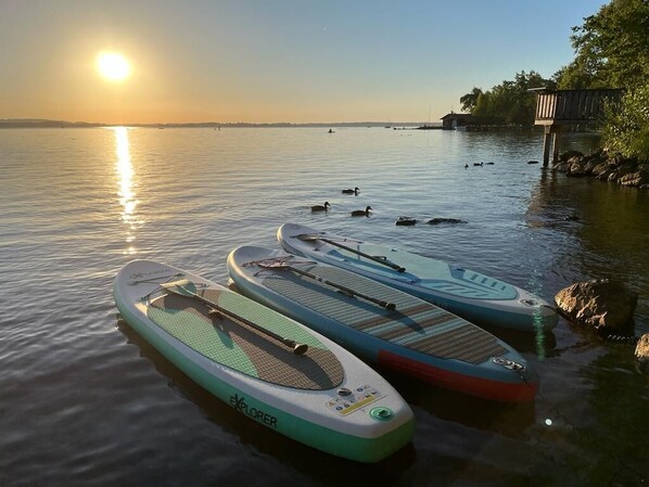 Drei Stand-Up-Paddleboards auf ruhigem Wasser in der Nähe eines Stegs, im Hintergrund ein Sonnenuntergang.