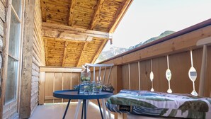 Een houten terras met een tafel, een bed, een raam en uitzicht op een berg.