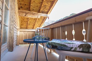 A wooden deck with a table and a bed, a window, and a view of a mountain.