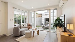 A modern living room with a sofa, coffee table, and a TV on a wooden stand. - Galatea Residence | Two Minutes to Beach and Town (Williamstown)
