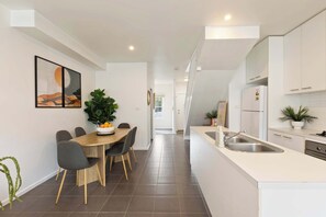 Uma cozinha moderna com armários brancos, uma ilha central com pia e um espaço de refeições com mesa e cadeiras.
