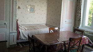 Une pièce comprenant un lit, une table, des chaises, un radiateur et une fenêtre avec des rideaux.