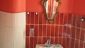 Une salle de bain avec un lavabo blanc, un miroir doté d’un cadre orné et des murs recouverts de carreaux rouges.
