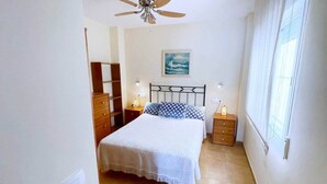 Ein Schlafzimmer mit einem Bett, einem Deckenventilator, einem Nachttisch, einer Kommode und einem Fenster.
