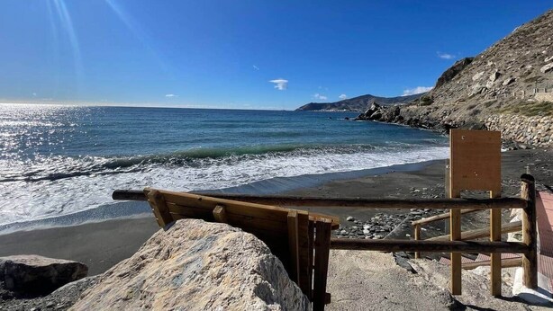 Ein Strand mit einer hölzernen Bank und einer Holzkonstruktion, vermutlich einem Rettungsschwimmerstand, mit Blick auf den Ozean.
