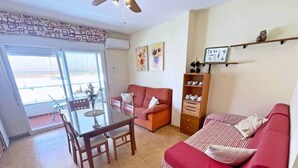 Ein Wohnzimmer mit einer Couch, einem Esstisch mit Stühlen, einem Deckenventilator und einer Glastür, die auf einen Balkon führt.