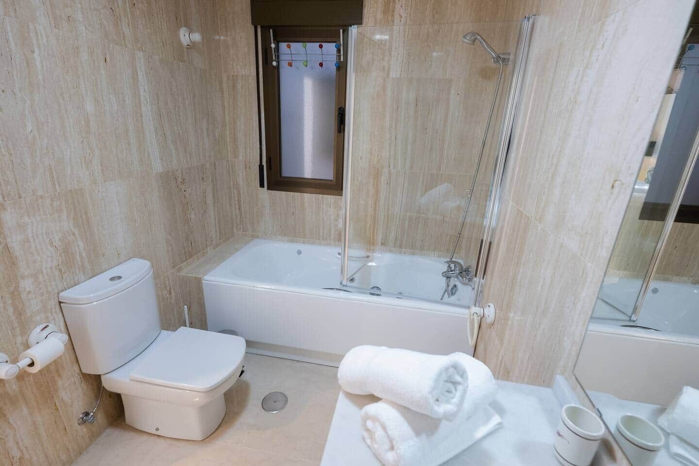 A bathroom with a toilet, bathtub, shower, and a towel on the counter.