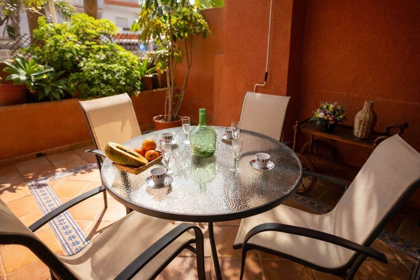 A round glass table with chairs, a fruit bowl, a bottle, and glasses.