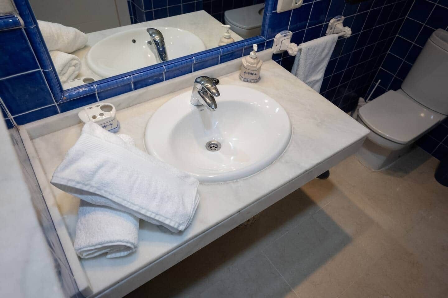 Un baño con lavamanos blanco, espejo y paredes con azulejos azules.