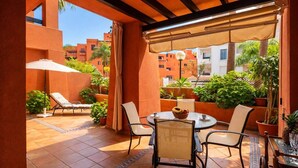Eine überdachte Terrasse im Freien mit einem runden Tisch, Stühlen und Topfpflanzen.