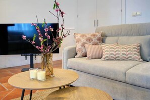 Un salon avec un canapé, des coussins à motifs, une table basse avec des bougies et un vase rempli de fleurs.