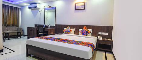 A modern hotel room with a large bed, a desk, a chair, a sofa, and a mirror.
