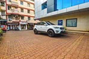 A white SUV parked on a paved area in front of a building with a sign indicating a 10% discount on Monday. - Hotel Shakti Palace (Ponda)