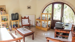 A cozy living room with a wooden chair, a small table, a bookshelf, a television, and a desk with a printer.