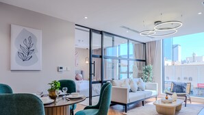 Ein modernes Wohnzimmer mit einer Couch, Sesseln, einem Esstisch und einem großen Fenster mit Blick auf die Stadt.