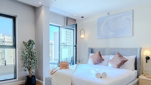 Ein modernes Hotelzimmer mit einem großen Bett, einer Topfpflanze, Blick auf die Stadt und minimalistischer Einrichtung.