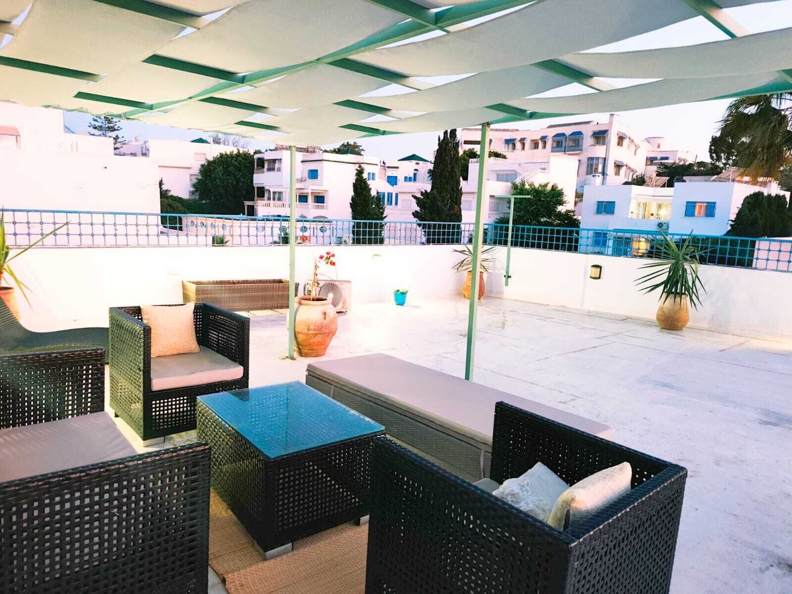 An outdoor patio with wicker furniture, a glass-top table, and potted plants.