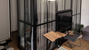 Ein Zimmer mit Glastrennwand, einem Fernseher, einem kleinen Tisch und einer Pflanze.