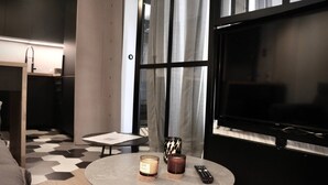 Ein stilvolles Zimmer mit einem runden Tisch, zwei Kerzen, einer Fernbedienung und einem großen Fernseher.