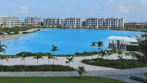 A resort with a large pool, palm trees, and multi-story buildings. - Modern 2Bdrm Apt Lagoon-Style Beach  Downtown (Punta Cana)