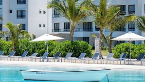 A hotel with a pool, sun loungers, palm trees, and a boat. - Modern 2Bdrm Apt Lagoon-Style Beach  Downtown (Punta Cana)