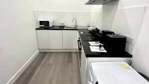 Una cocina compacta con armarios blancos, un microondas, una cafetera y un tostador.