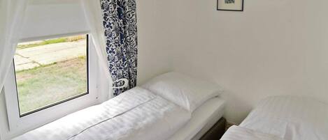 Ein Zimmer mit zwei Betten, einem Fenster mit Vorhängen und zwei gerahmten Bildern an der Wand.