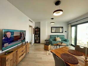 Ein Wohnzimmer mit Fernseher, Sofa, Couchtisch und Essbereich.
