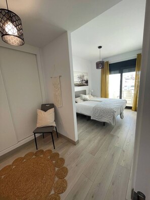 Ein modernes Schlafzimmer mit Bett, Stuhl, Pendelleuchte und Blick ins Freie.