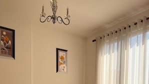 A bedroom with a bed, a chandelier, curtains, and two framed pictures on the wall. - Stay in a comfortable apartment - Valentino Apartment (Shkodër)