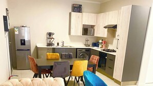 Ett kompakt bostadsutrymme med en soffa, ett matbord, stolar, ett soffbord och ett litet kök.
