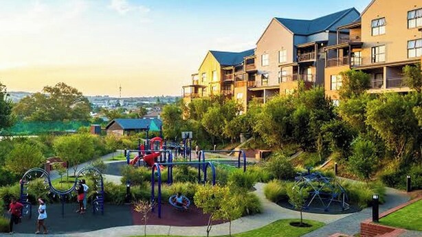 Un parc infantil amb diverses estructures de jocs envoltat d'una gespa ben cuidada i passeres.