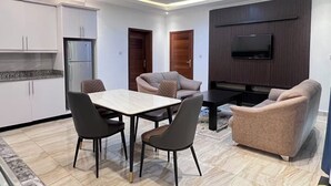 Ein modernes Wohnzimmer mit Essbereich, einer Küche und einem an einer Holzvertäfelung befestigten Fernseher.