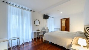 Een slaapkamer met een bed, bureau, stoel, televisie en raam met gordijnen.