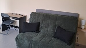 En grön soffa med svarta kuddar, ett litet skrivbord med en stol och en lampa på ett bord.