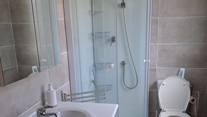 Ett modernt badrum med en dusch som är avskärmad med glasväggar, en vit tvättställ och en toalett.