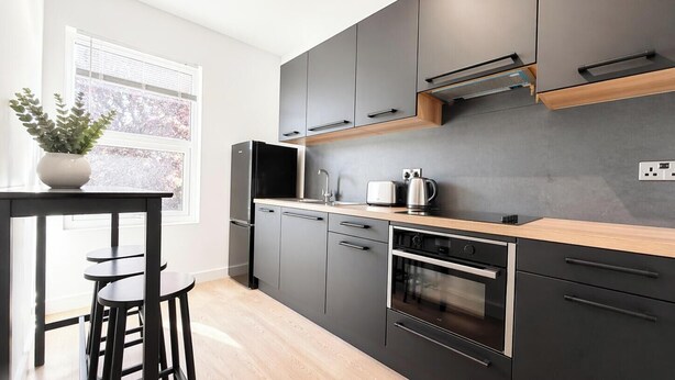 A modern kitchen with dark cabinets, a wooden countertop, a built-in oven, and a sink. - Exclusive Studio in the Heart of Hounslow! (Greater London)
