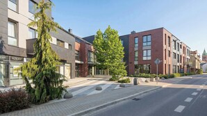 Ein modernes Gebäude mit einer Fassade aus Backstein und Glas, einer Fußgängerüberweg und einer von Bäumen gesäumten Straße.