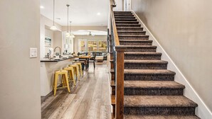 Una escalera de madera con barandilla que lleva a un comedor con techos altos y lámparas colgantes.