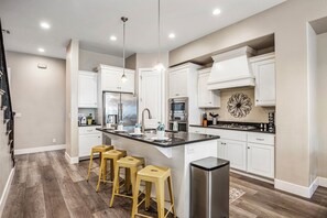 A modern kitchen with white cabinetry, stainless steel appliances, a central island with stools, and a decorative wall piece. - Coral Ridge 2076, Near Golf Course, Community Amenities! (Washington)