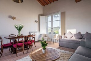 Ein Wohnzimmer mit einem Holzesstisch, roten Polsterstühlen, einem grauen Sofa und einer Zimmerpflanze auf einem runden Couchtisch.