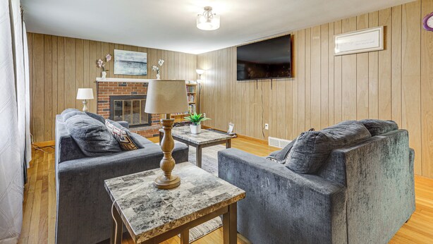 Ein Wohnzimmer mit Kamin, zwei grauen Sofas, einem kleinen Tisch und einem an der Wand befestigten Fernseher.
