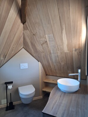 A modern bathroom with a wooden sloped ceiling, a white toilet, a round sink, and a shower area. - Renovated to make your stay "just like home". Pets allowed! (Nonards)